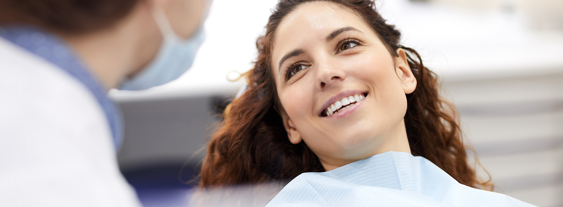 The image features a woman with a broad smile in a dental office, seated in the dentist s chair while receiving treatment.