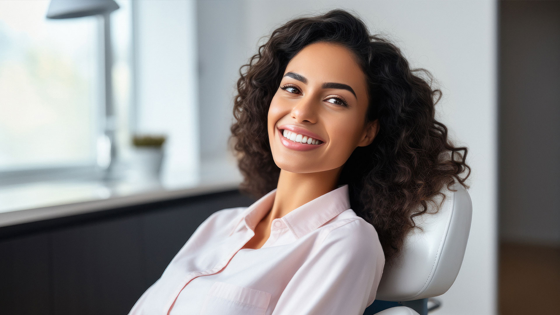 A woman with a radiant smile, seated in an office chair, smiling broadly at the camera.