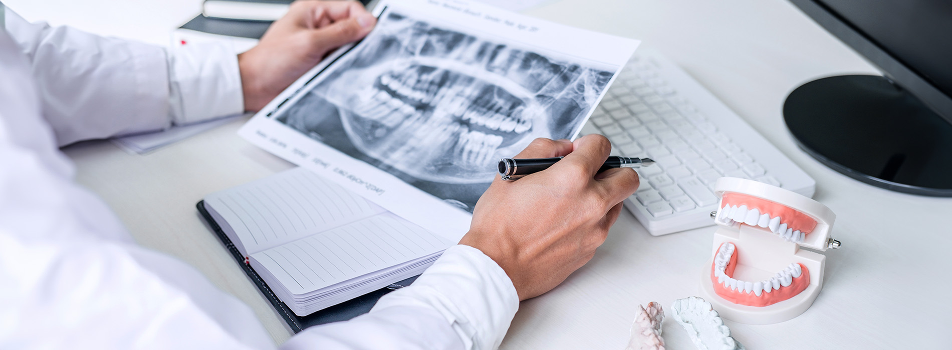 A dental professional examining a digital X-ray of a patient s teeth, sitting at a desk with medical equipment and paperwork.