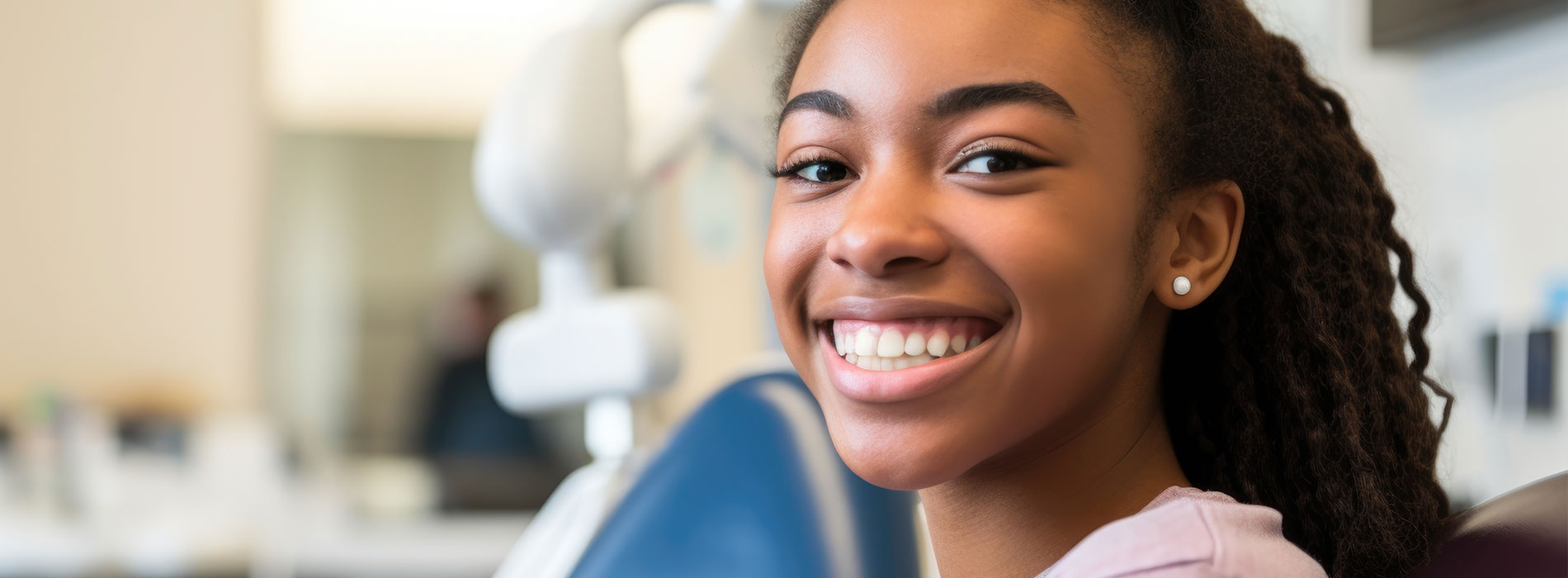 The image shows a young person with a smile, sitting in front of a dental chair, likely at a dentist s office.