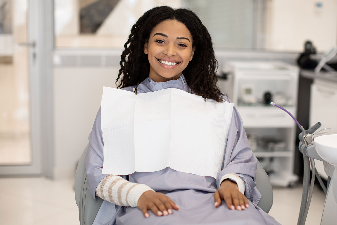 A woman in a dental chair, smiling, with a mouthguard on her teeth.