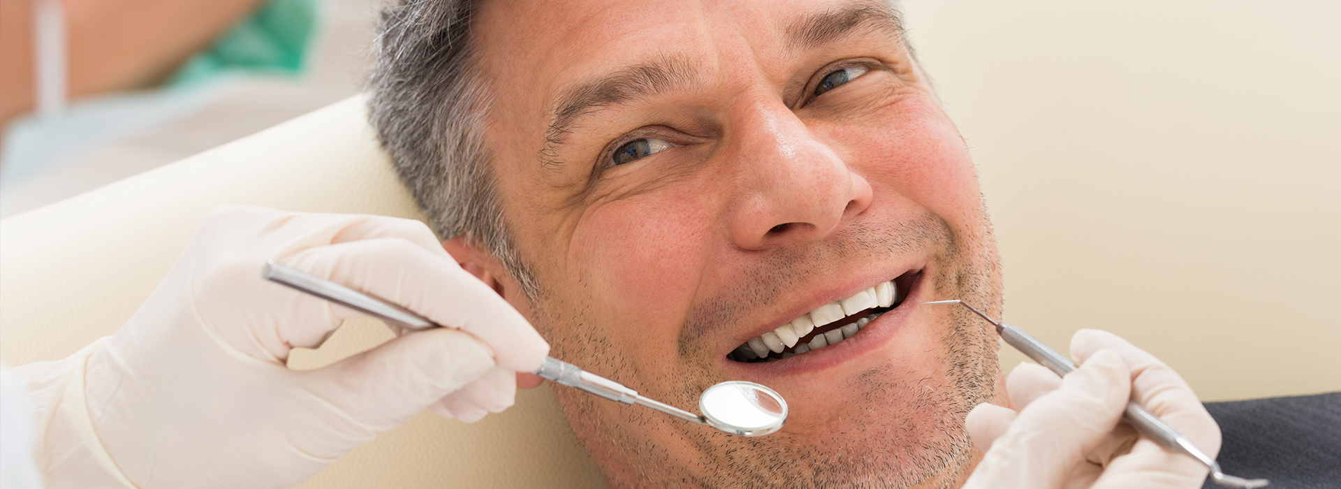 A man is seated in a dental chair, receiving dental care from a dentist who is performing a procedure using dental tools.