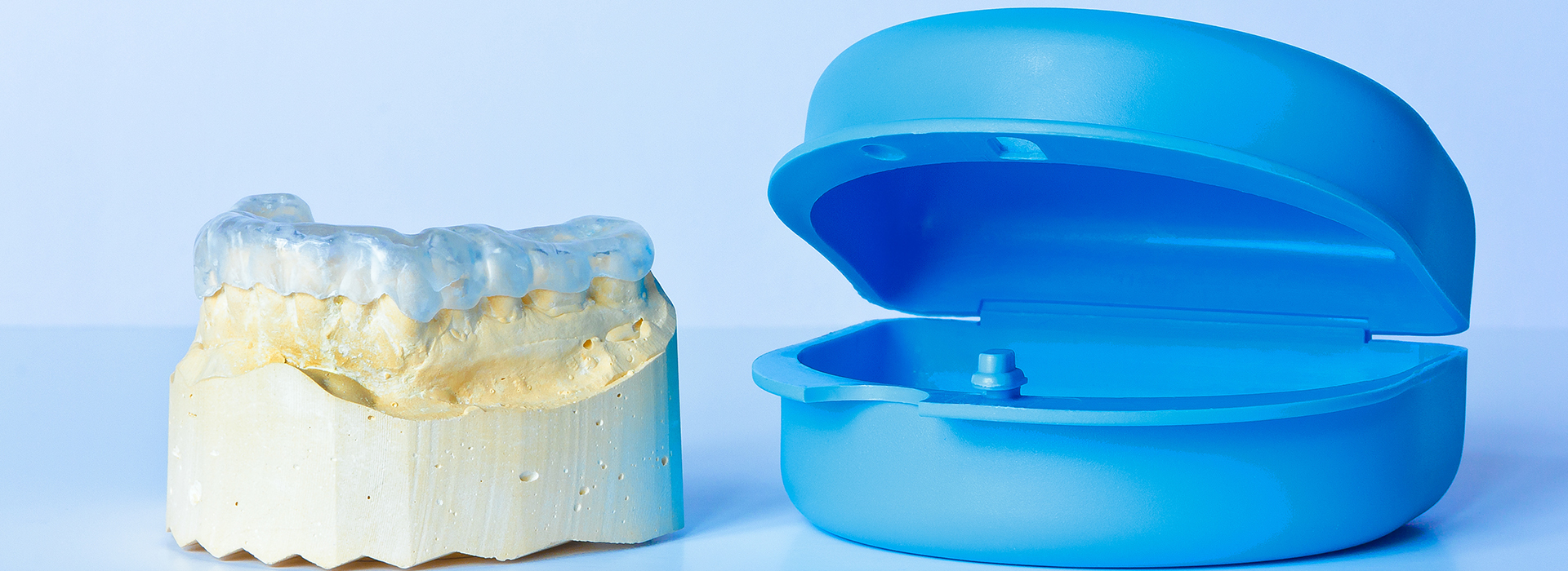 The image displays a blue plastic dental model on the right and a yellow dental model on the left, both placed on a white surface.