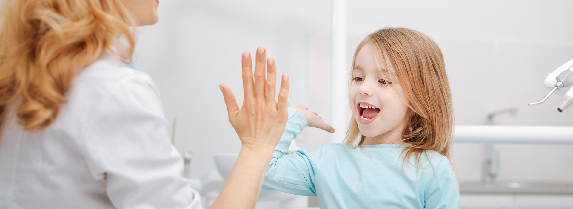 This is a photograph of an adult woman and a young girl in a dental setting, with the woman s hand raised towards the child.