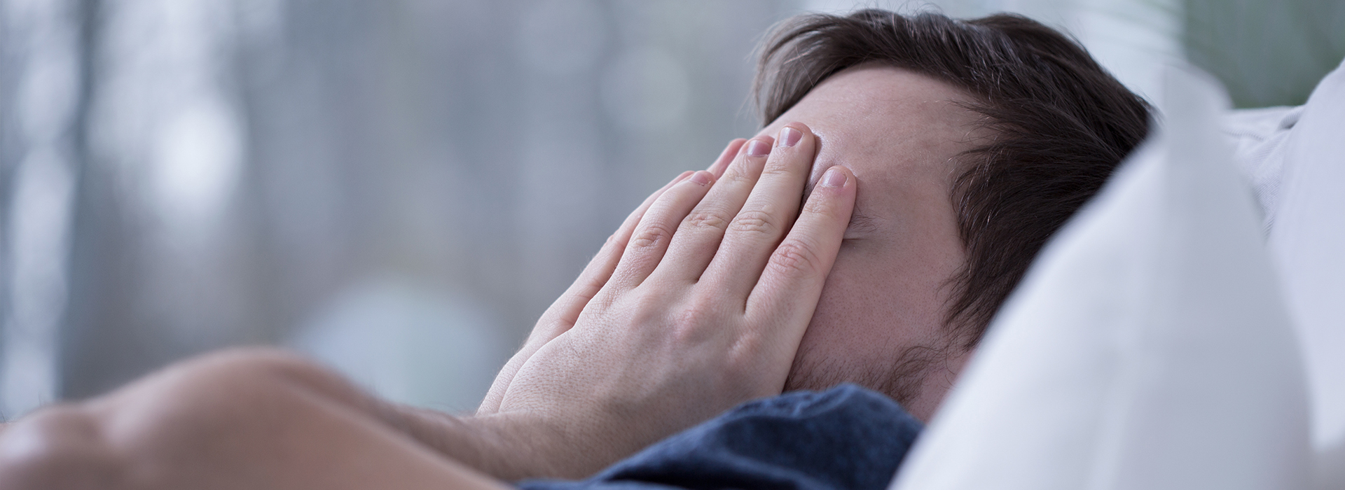 The image shows a person lying in bed with their hands covering their face, appearing to be in a state of distress or sadness.