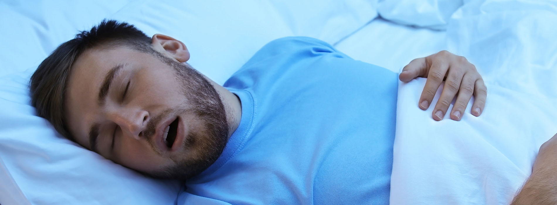 A man is lying in bed with his eyes closed, wearing a blue shirt.