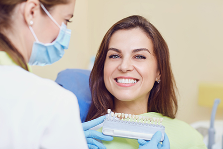 A dental hygienist is assisting a woman in a dentist s office, with the woman smiling and seated in a chair while the dental hygienist stands behind her.