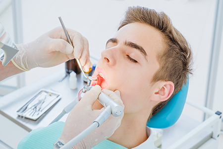 The image depicts a dental clinic scene with a patient seated in the chair, receiving dental care from a dentist who is performing a procedure on their teeth.