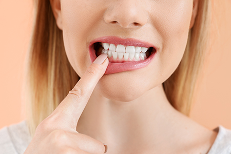 A young woman with her finger on her teeth, smiling and holding a finger up to her mouth.