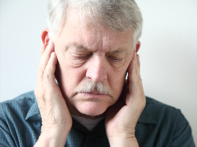 A man with gray hair, wearing a green shirt, is seen from the back and has his hand on his face as if he s rubbing his cheek or holding his nose.